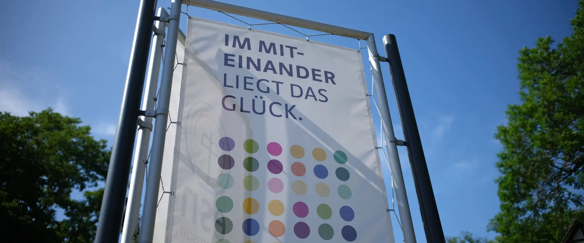 Fahne mit Text "Im Miteinader liegt das Glück" und bunten Punkten