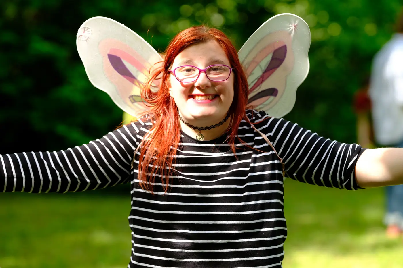 Mädchen lacht mit ausgebreiteten Armen in die Kamera, sie trägt Schmetterlingsflügel