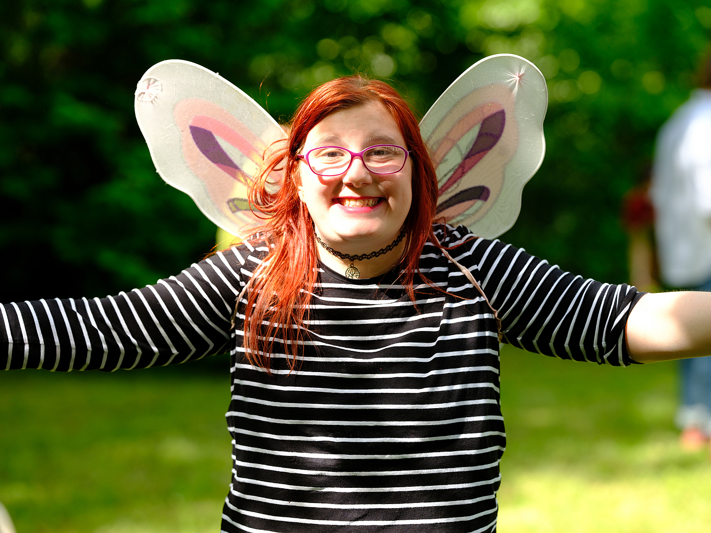 Mädchen lacht mit ausgebreiteten Armen in die Kamera, sie trägt Schmetterlingsflügel